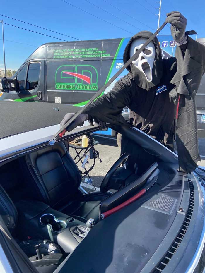 Halloween-costumed technician beside an empty vehicle windshield opening