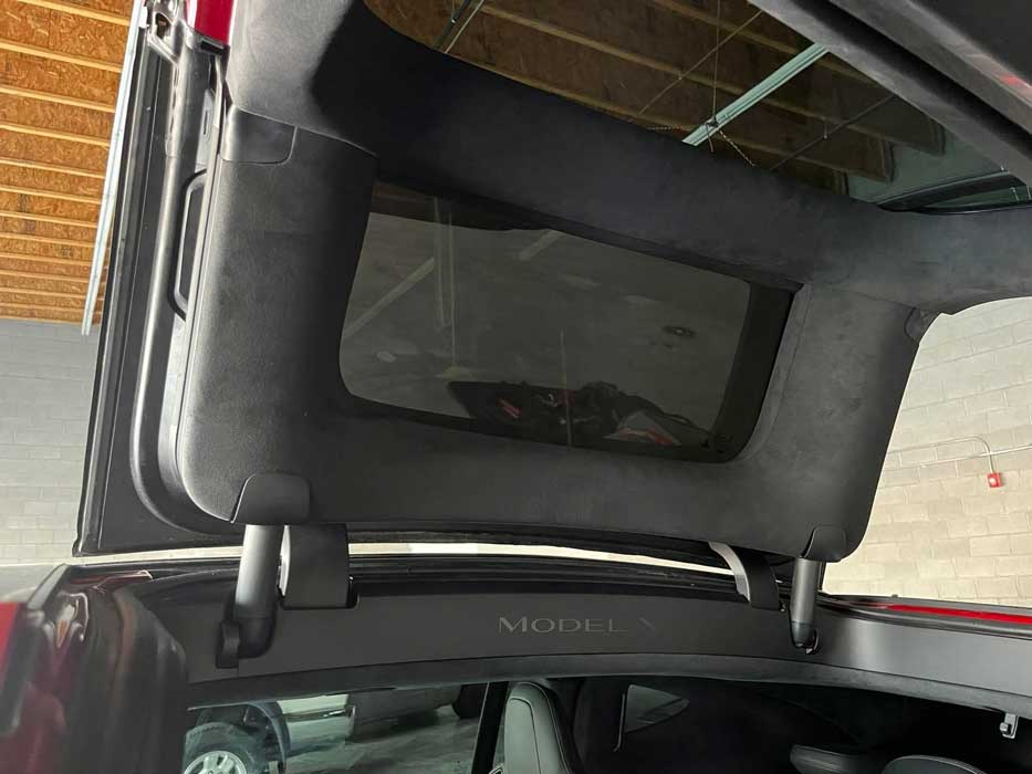 Underside of a raised Tesla Model X falcon-wing door during glass service