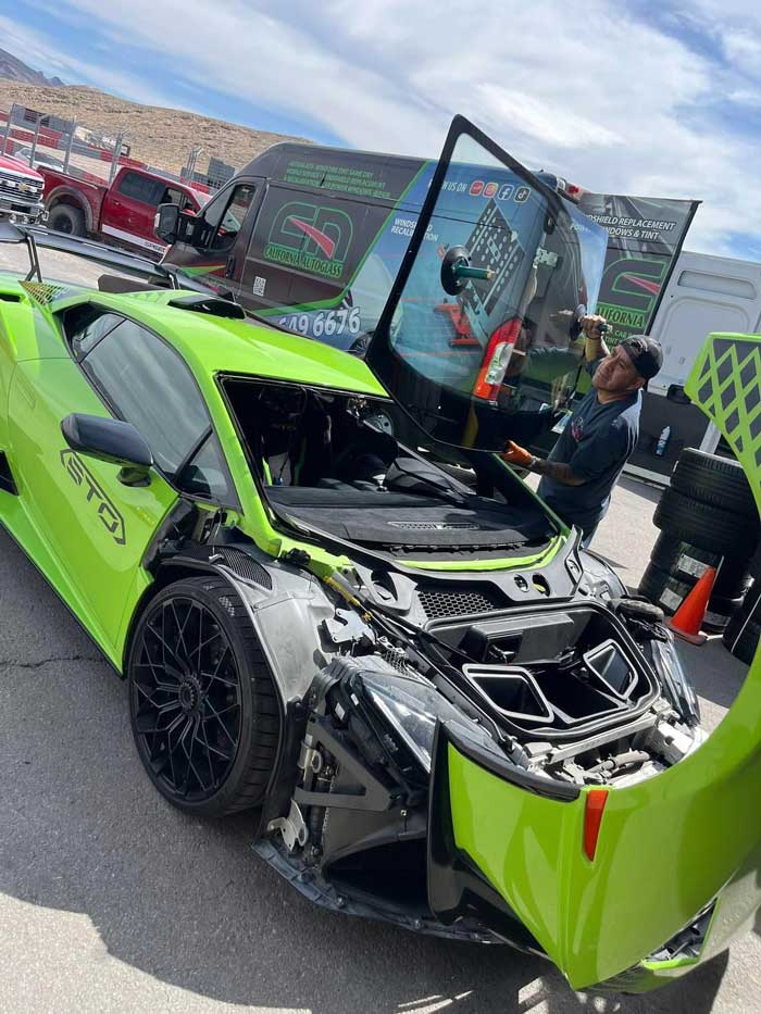 Technician holding a replacement windshield above a green Lamborghini Huracán STO