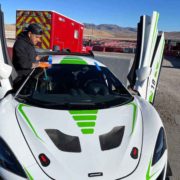 Technician fitting a windshield to a white and green McLaren race car