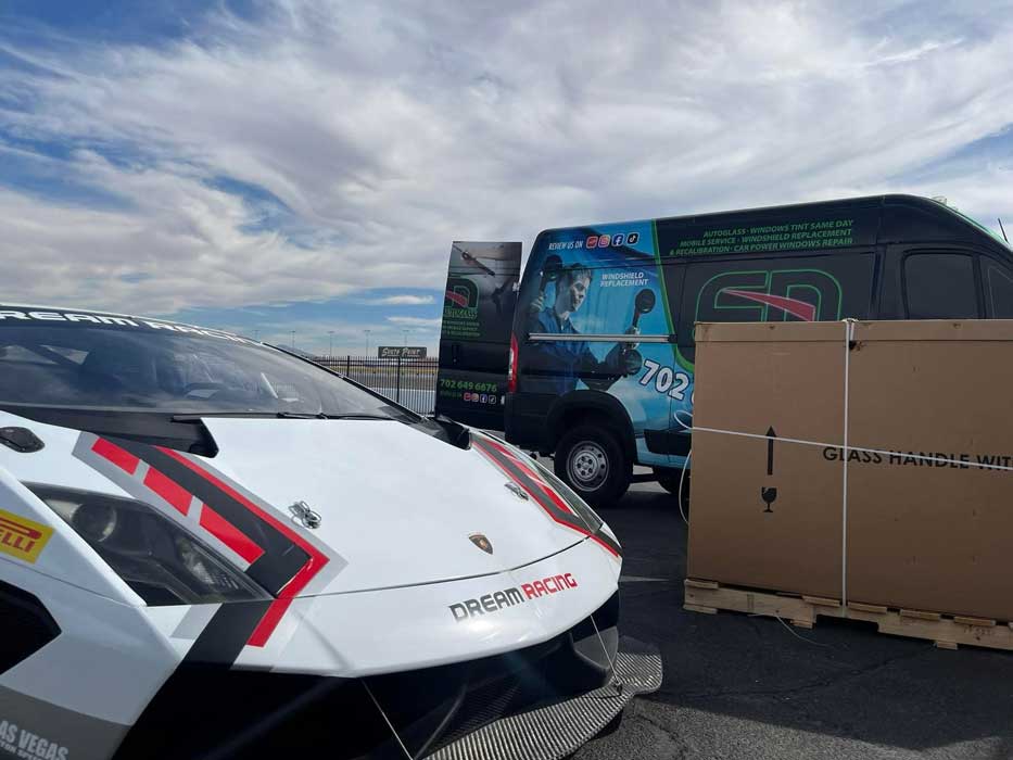 Completed white Lamborghini beside a mobile auto glass service van