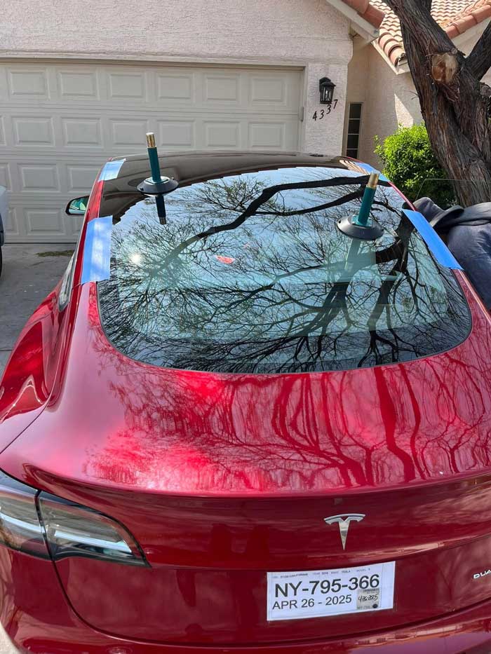 Rear glass positioned on a red Tesla Model Y with suction handles