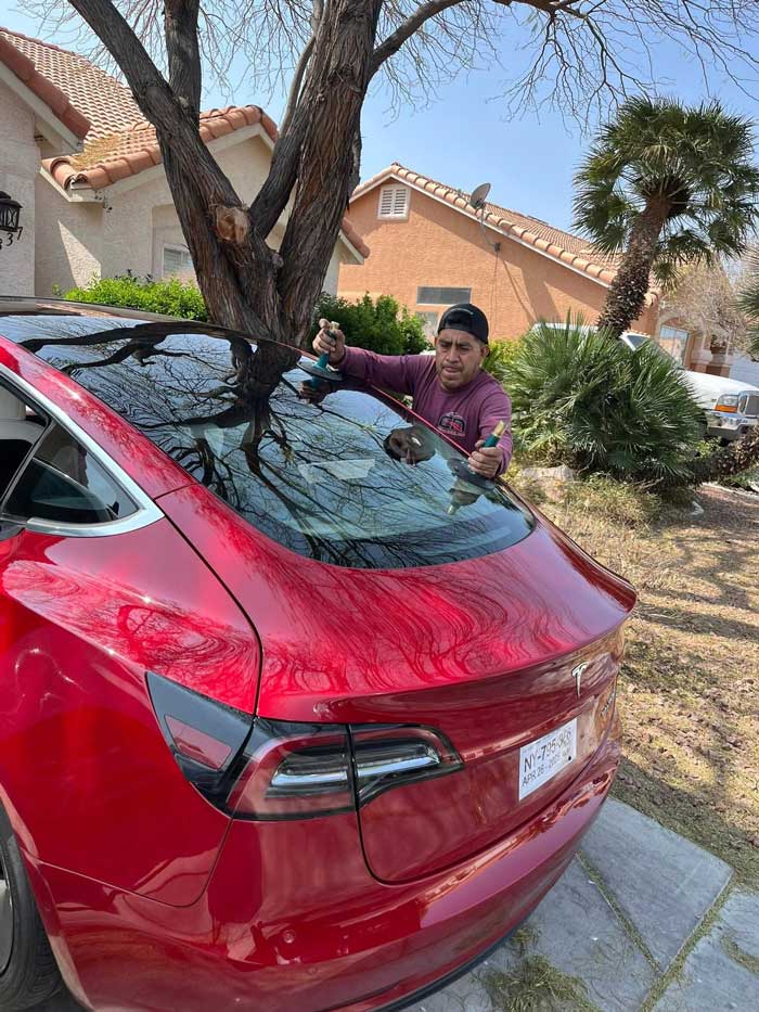 Technician setting rear hatch glass on a red Tesla Model Y